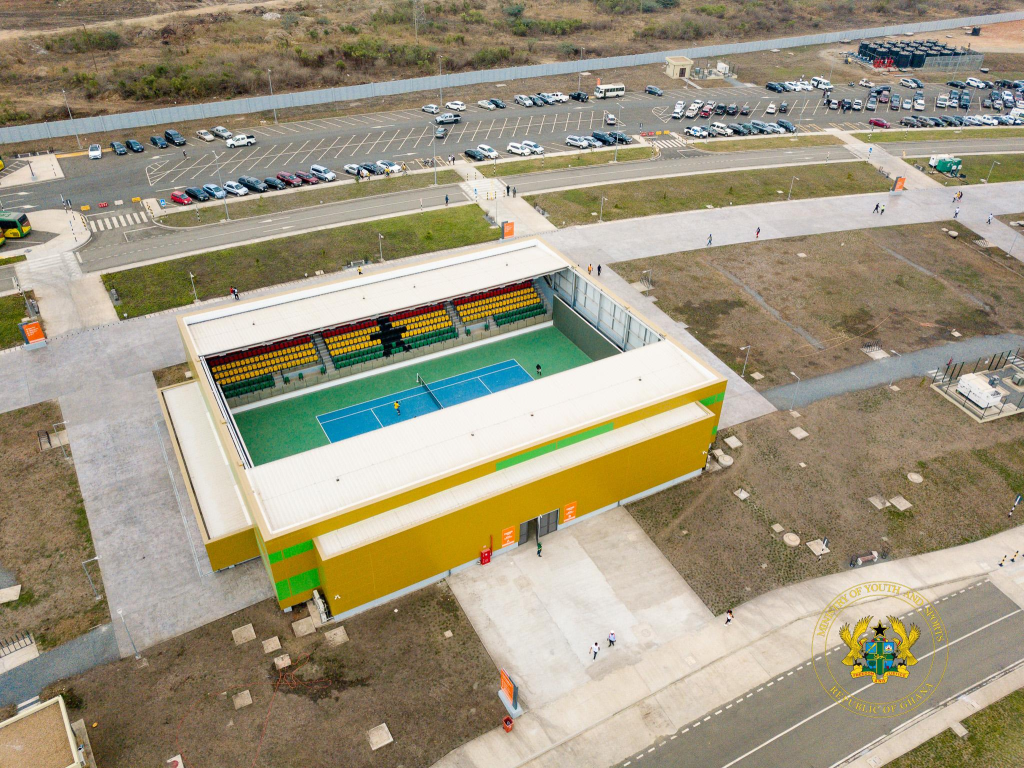 Havadan çekilmiş bir görüntüde, modern bir tenis sahası bulunan spor merkezi görünmektedir. Merkezin etrafında boş alanlar, otopark ve yürüyüş yolları bulunuyor.